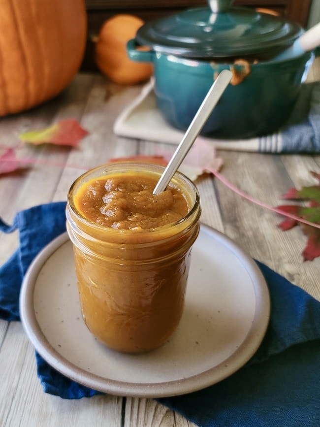 This photo shows a mason jar filled with pumpkin butter with a spoon. 