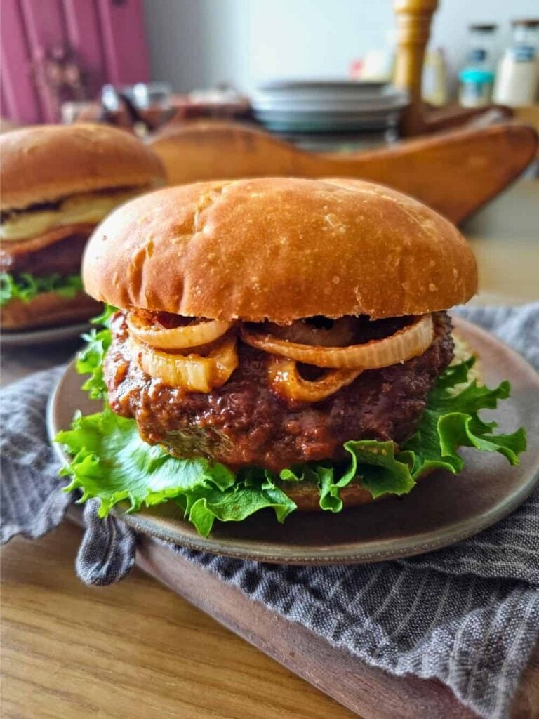 Burger with lettuce, beef patty, and onion rings on a plate.