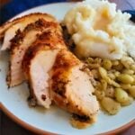Sliced roasted chicken with herbs beside mashed potatoes and seasoned potato gnocchi on a plate.