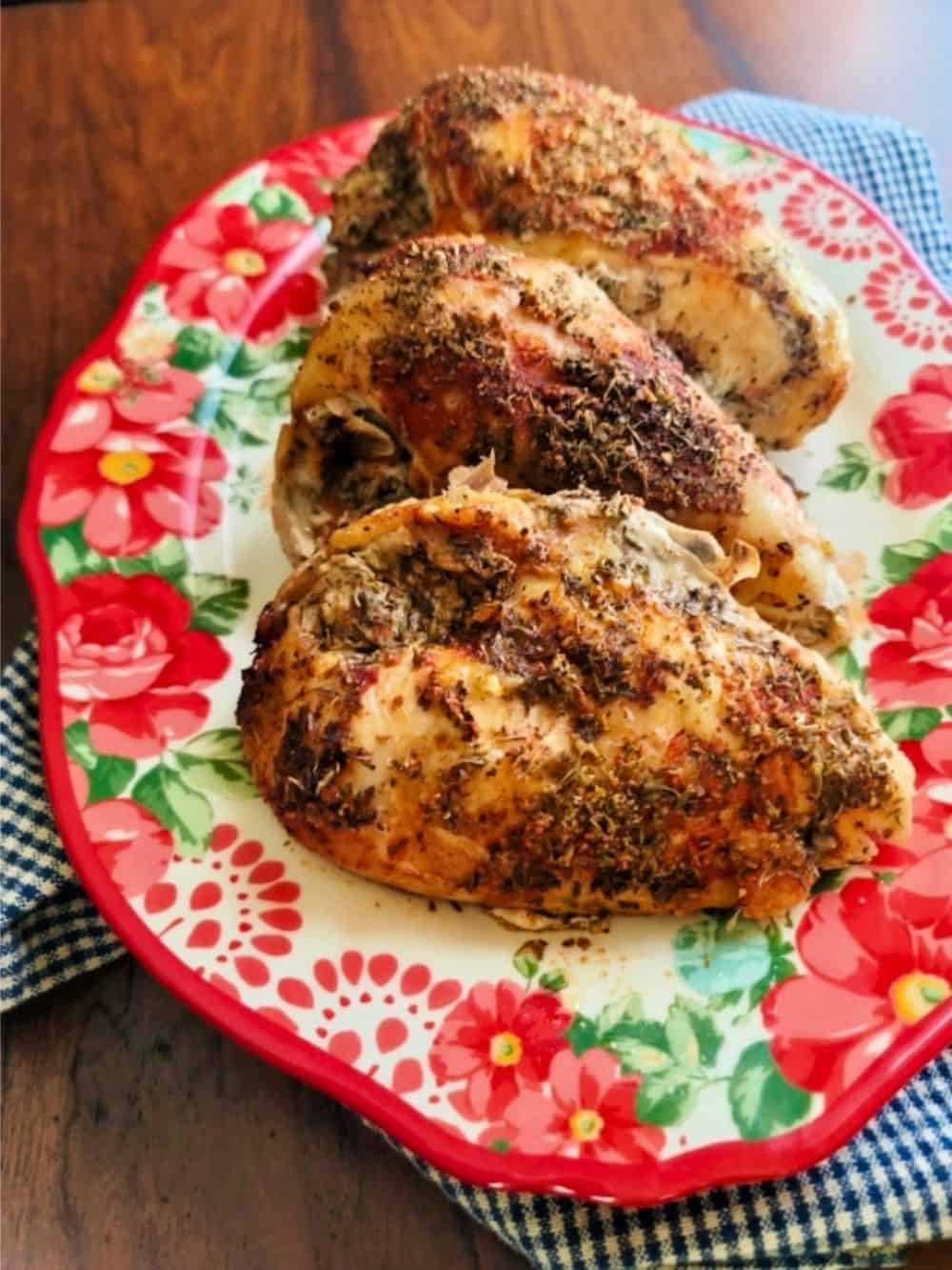 Herb-crusted roast chicken pieces on a floral red plate.