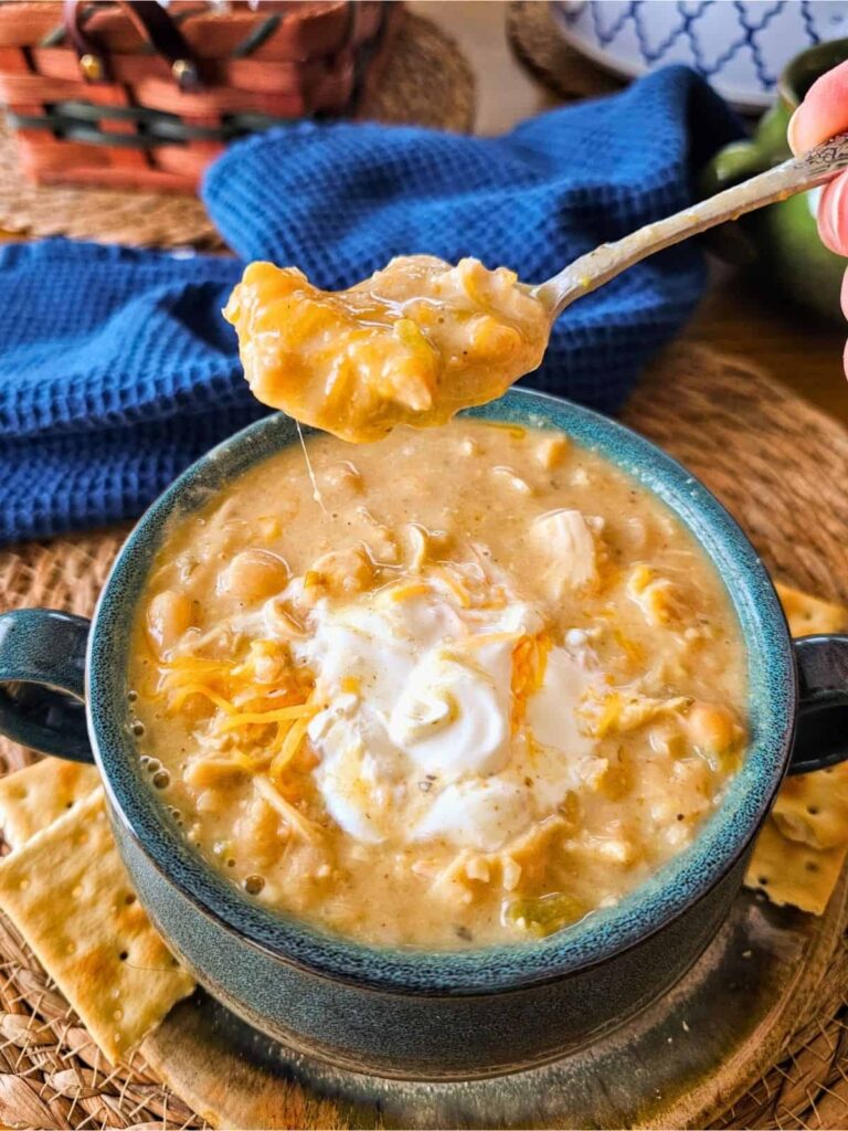 Creamy chicken tortilla soup in a teal bowl topped with sour cream and shredded cheese, spoon lifting a chunky tortilla bite.