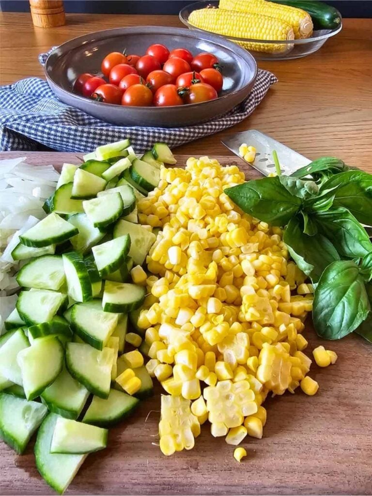 Vegetables on a cutting board for corn and cucumber salad ingredients.