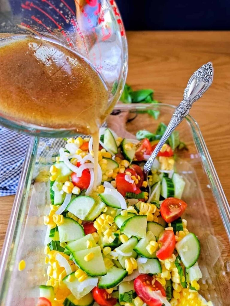Pouring dressing on a bowl of Corn Cucumber Salad with Fresh Basil and Cherry Tomatoes.