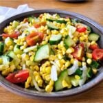 Bowl of colorful vegetable salad with corn, cucumber, tomatoes, and onions on a wooden table.