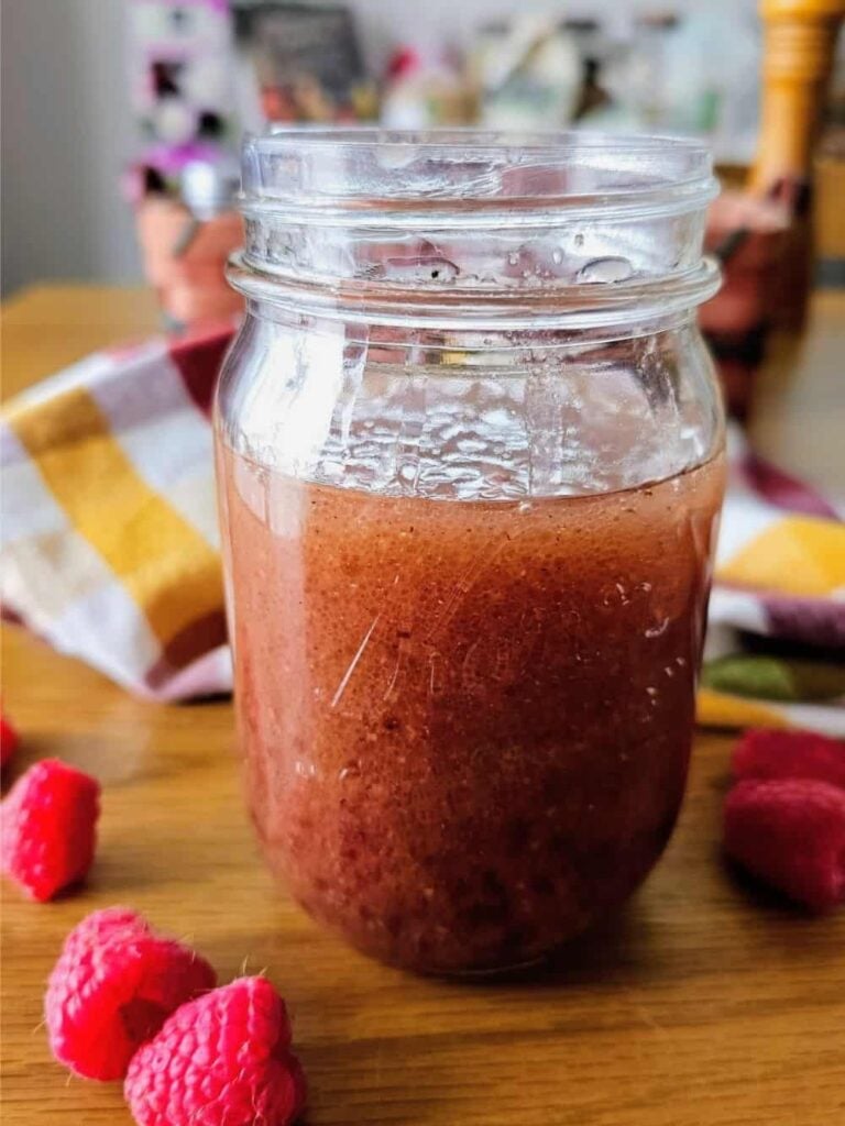 Mason jar with thick chocolate smoothie on a wooden table, raspberries in the foreground.